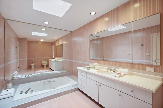 full bathroom with vanity, toilet, a skylight, a whirlpool tub, and tile walls