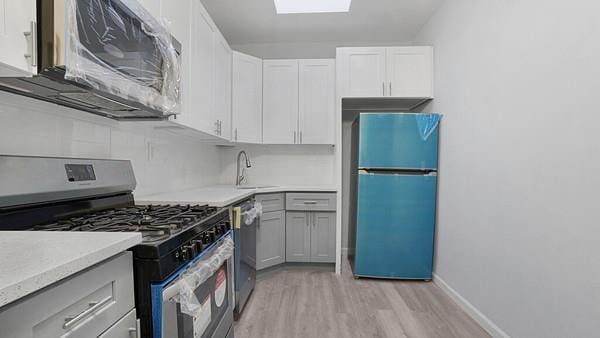 kitchen with appliances with stainless steel finishes, sink, white cabinetry, a skylight, and light hardwood / wood-style floors