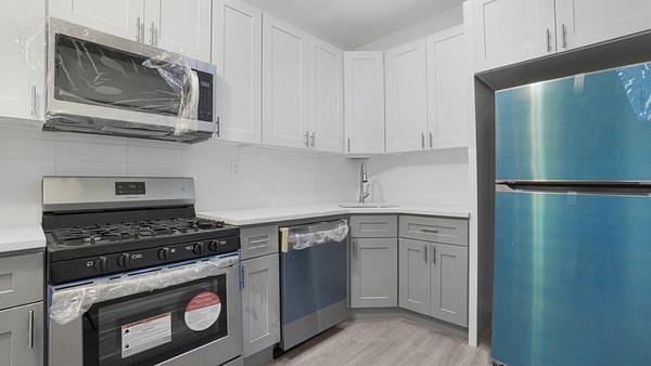 kitchen featuring gray cabinets, white cabinetry, stainless steel appliances, and sink