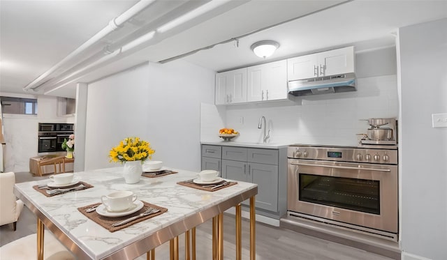 kitchen featuring range, gray cabinetry, light hardwood / wood-style flooring, tasteful backsplash, and oven