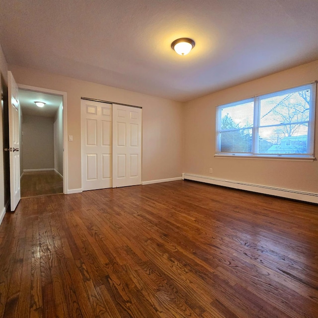 unfurnished bedroom featuring dark hardwood / wood-style flooring, baseboard heating, and a closet