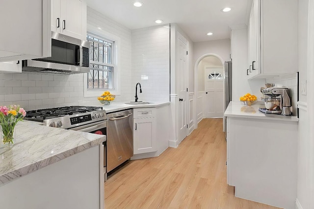 kitchen with light wood-type flooring, appliances with stainless steel finishes, white cabinets, and a sink