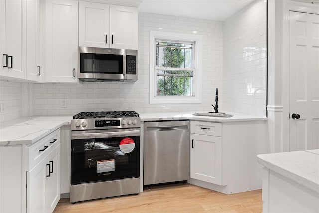 kitchen with decorative backsplash, appliances with stainless steel finishes, light wood-type flooring, white cabinetry, and a sink