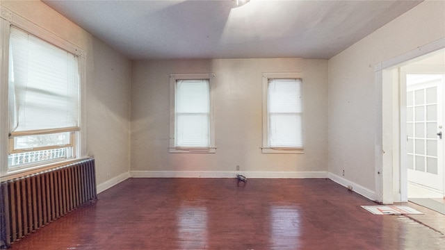 empty room featuring dark wood-type flooring, a wealth of natural light, radiator, and baseboards