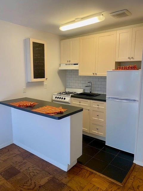 kitchen with sink, range, kitchen peninsula, white fridge, and white cabinets