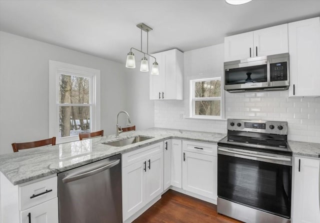 kitchen with appliances with stainless steel finishes, decorative light fixtures, sink, white cabinets, and kitchen peninsula