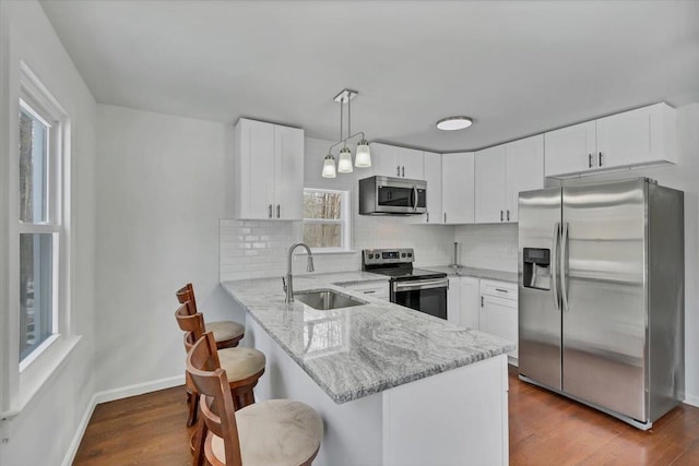 kitchen with decorative light fixtures, white cabinetry, sink, kitchen peninsula, and stainless steel appliances