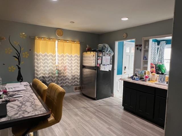 kitchen with dark cabinets, visible vents, light wood-style floors, light countertops, and freestanding refrigerator