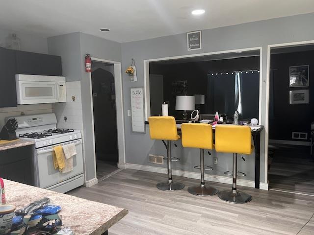 kitchen with light countertops, wood finished floors, white appliances, dark cabinetry, and baseboards