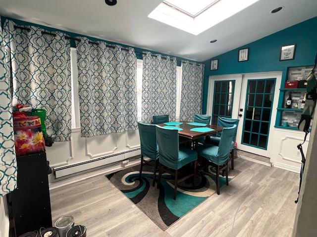 dining room featuring lofted ceiling with skylight, baseboard heating, wood finished floors, and french doors