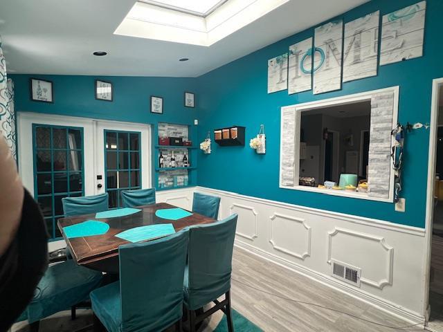 dining space featuring a wainscoted wall, vaulted ceiling with skylight, french doors, and visible vents