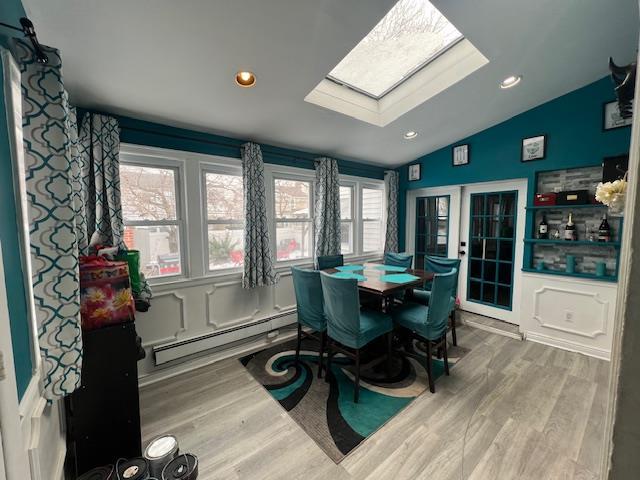 dining room with vaulted ceiling with skylight, baseboard heating, wood finished floors, and recessed lighting