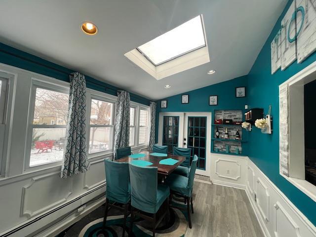 dining room featuring a baseboard heating unit, vaulted ceiling with skylight, recessed lighting, and wood finished floors