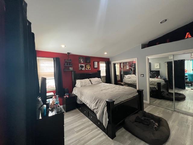 bedroom featuring light wood-style floors, recessed lighting, vaulted ceiling, and two closets