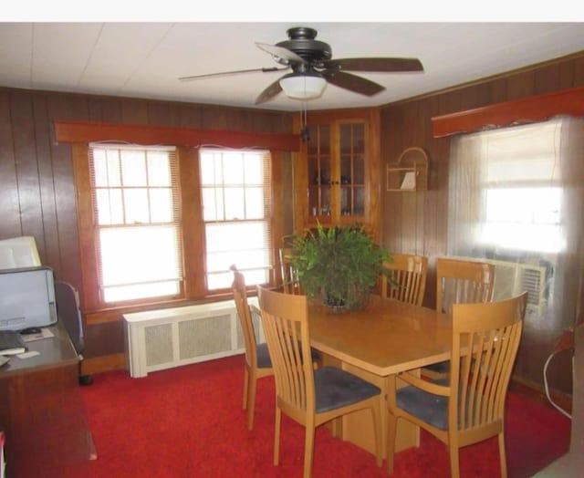 carpeted dining area featuring radiator, wooden walls, and ceiling fan