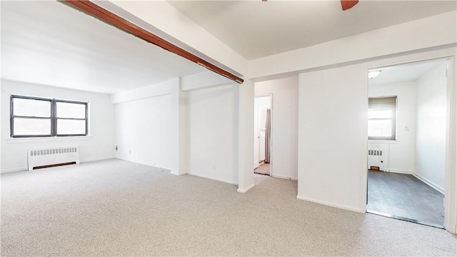 unfurnished room with beam ceiling, radiator, and light carpet