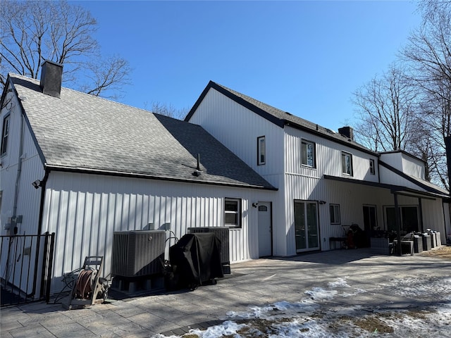 rear view of house with a shingled roof, a patio area, central AC, and a chimney