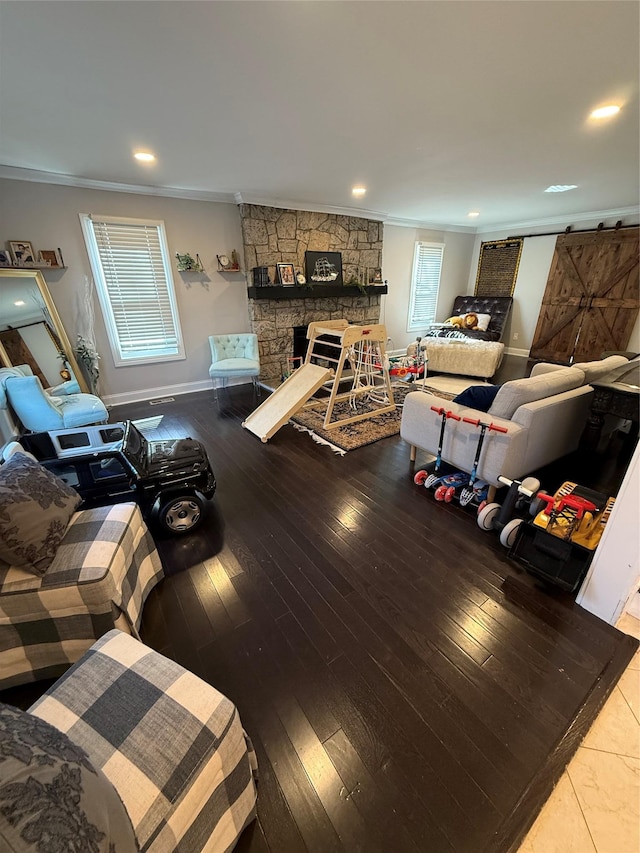 living area with a barn door, hardwood / wood-style flooring, a fireplace, baseboards, and crown molding