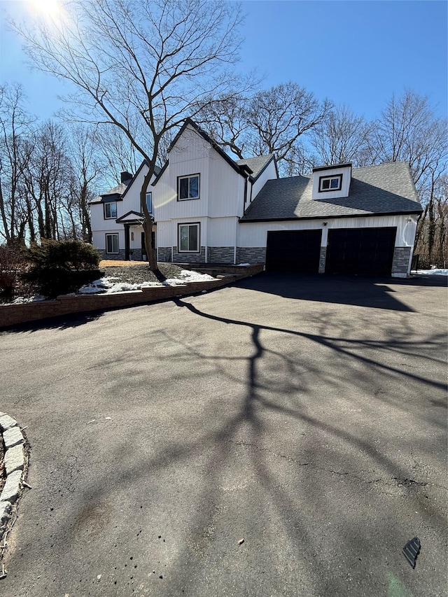 view of front of house with stone siding, roof with shingles, an attached garage, and driveway