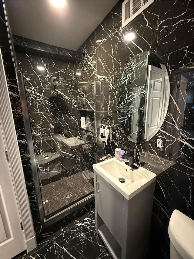 bathroom featuring toilet, vanity, tile walls, marble finish floor, and a shower stall