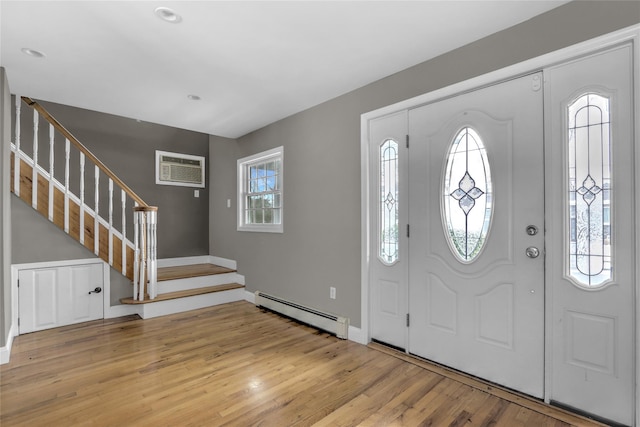 foyer entrance with light wood-type flooring, a wall unit AC, and a baseboard radiator