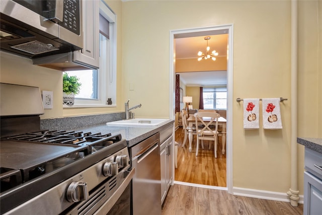 kitchen featuring appliances with stainless steel finishes, pendant lighting, sink, an inviting chandelier, and light hardwood / wood-style flooring