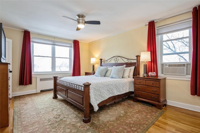 bedroom featuring cooling unit, multiple windows, radiator heating unit, and light wood-type flooring