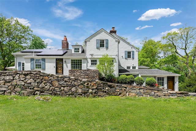 58 Spring Ln, Chappaqua, NY 10514 - rear view of house featuring a chimney, roof mounted solar panels, a yard, and stucco siding