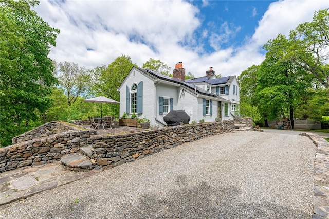 58 Spring Ln, Chappaqua, NY 10514 - view of side of home featuring a chimney, a patio area, solar panels, stucco siding, and outdoor dining area