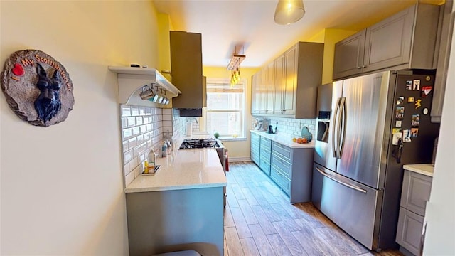 kitchen featuring gray cabinets, backsplash, stove, stainless steel refrigerator with ice dispenser, and light wood-type flooring