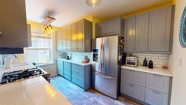 kitchen with gray cabinets, backsplash, stove, stainless steel refrigerator with ice dispenser, and light wood-type flooring