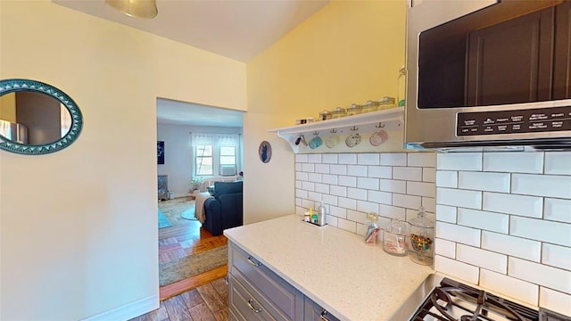 kitchen with decorative backsplash, gray cabinets, light stone countertops, and stovetop