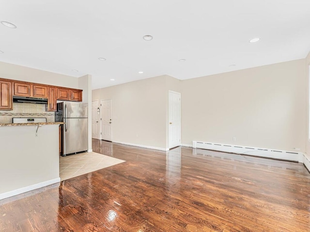 kitchen with stainless steel refrigerator, baseboard heating, tasteful backsplash, and light wood-type flooring