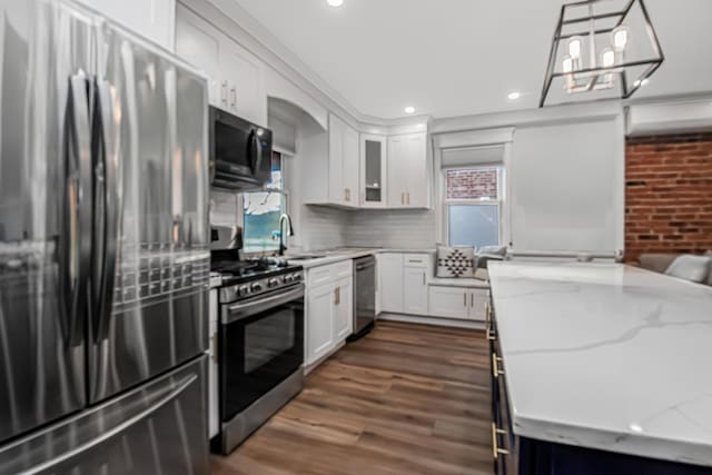 kitchen featuring white cabinets, hanging light fixtures, light stone counters, stainless steel appliances, and dark wood-type flooring