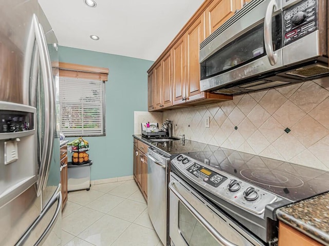 kitchen with sink, dark stone countertops, backsplash, light tile patterned floors, and stainless steel appliances