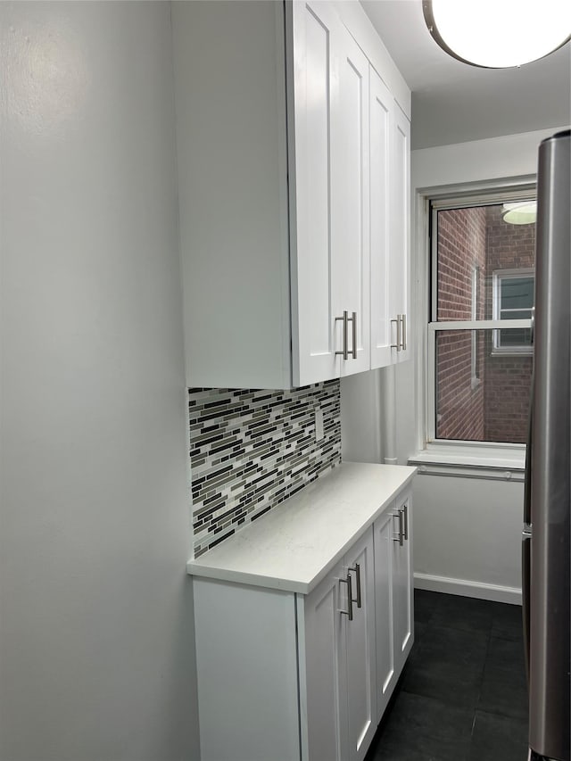 interior space featuring white cabinetry, backsplash, stainless steel refrigerator, and dark tile patterned flooring