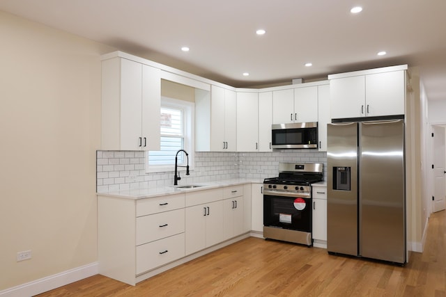 kitchen with appliances with stainless steel finishes, sink, white cabinets, backsplash, and light wood-type flooring