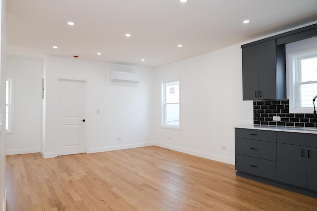 kitchen featuring a wall mounted AC, sink, light hardwood / wood-style flooring, and backsplash