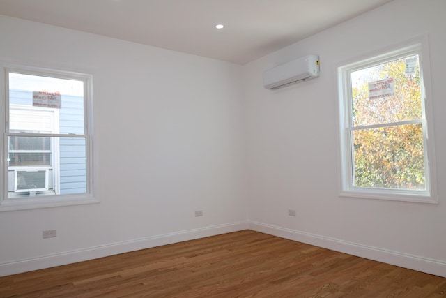 spare room featuring cooling unit, a wall mounted air conditioner, hardwood / wood-style flooring, and plenty of natural light