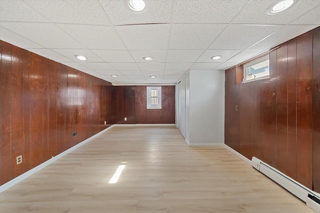 basement featuring light hardwood / wood-style flooring, a paneled ceiling, wood walls, and baseboard heating