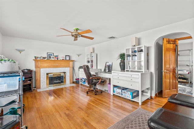 office space featuring light wood finished floors, arched walkways, visible vents, ceiling fan, and a premium fireplace