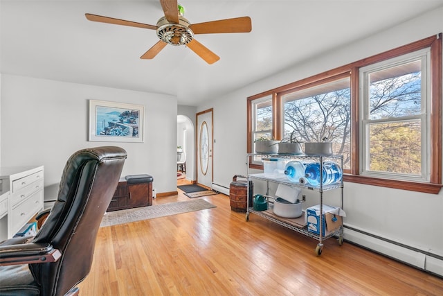 home office featuring arched walkways, baseboard heating, baseboards, and light wood-style floors