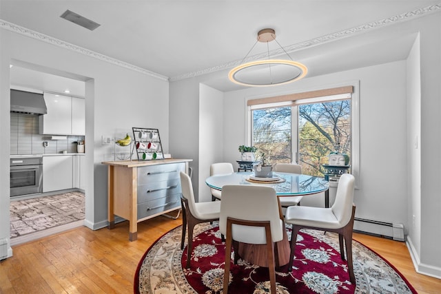 dining space featuring a baseboard radiator, baseboards, and light wood-style flooring