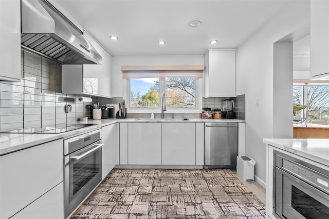 kitchen featuring white cabinets, modern cabinets, stainless steel appliances, wall chimney range hood, and a sink