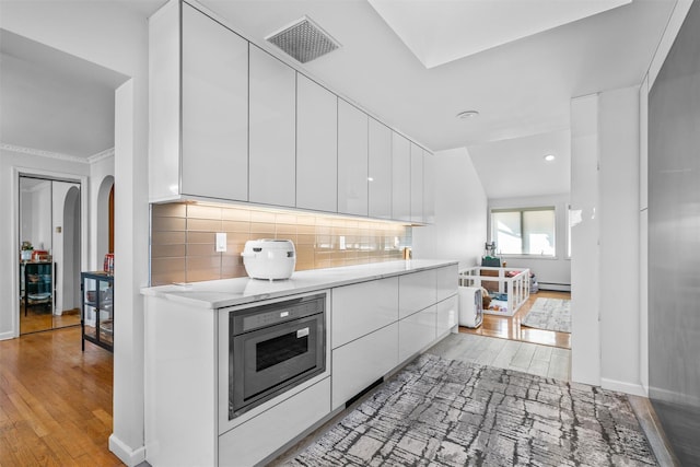 kitchen with arched walkways, oven, visible vents, white cabinetry, and light countertops