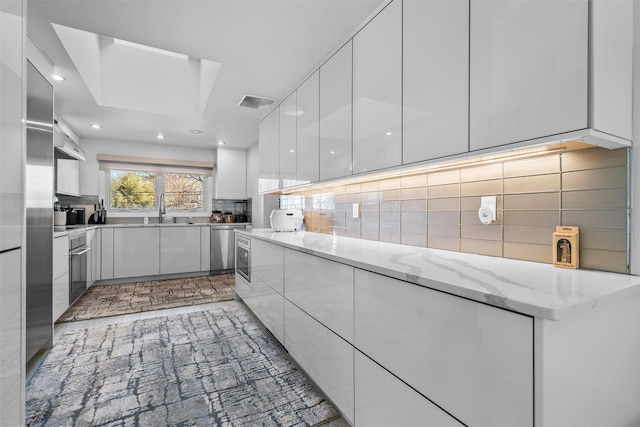 kitchen with a sink, visible vents, white cabinetry, tasteful backsplash, and modern cabinets