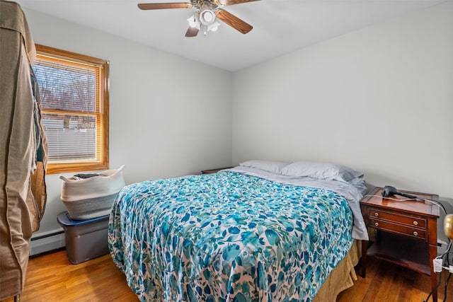 bedroom with ceiling fan, baseboard heating, and wood finished floors