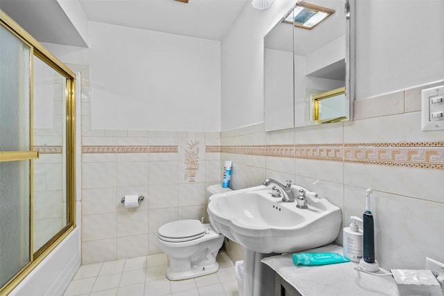 full bath with tile walls, toilet, combined bath / shower with glass door, a sink, and tile patterned flooring