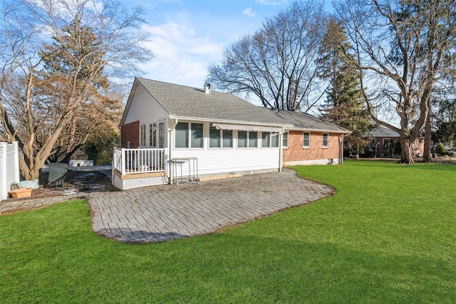 back of property with a lawn, a patio, a sunroom, roof with shingles, and brick siding