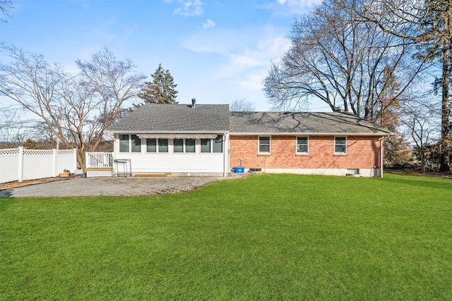 rear view of property with a patio, brick siding, fence, a lawn, and roof with shingles